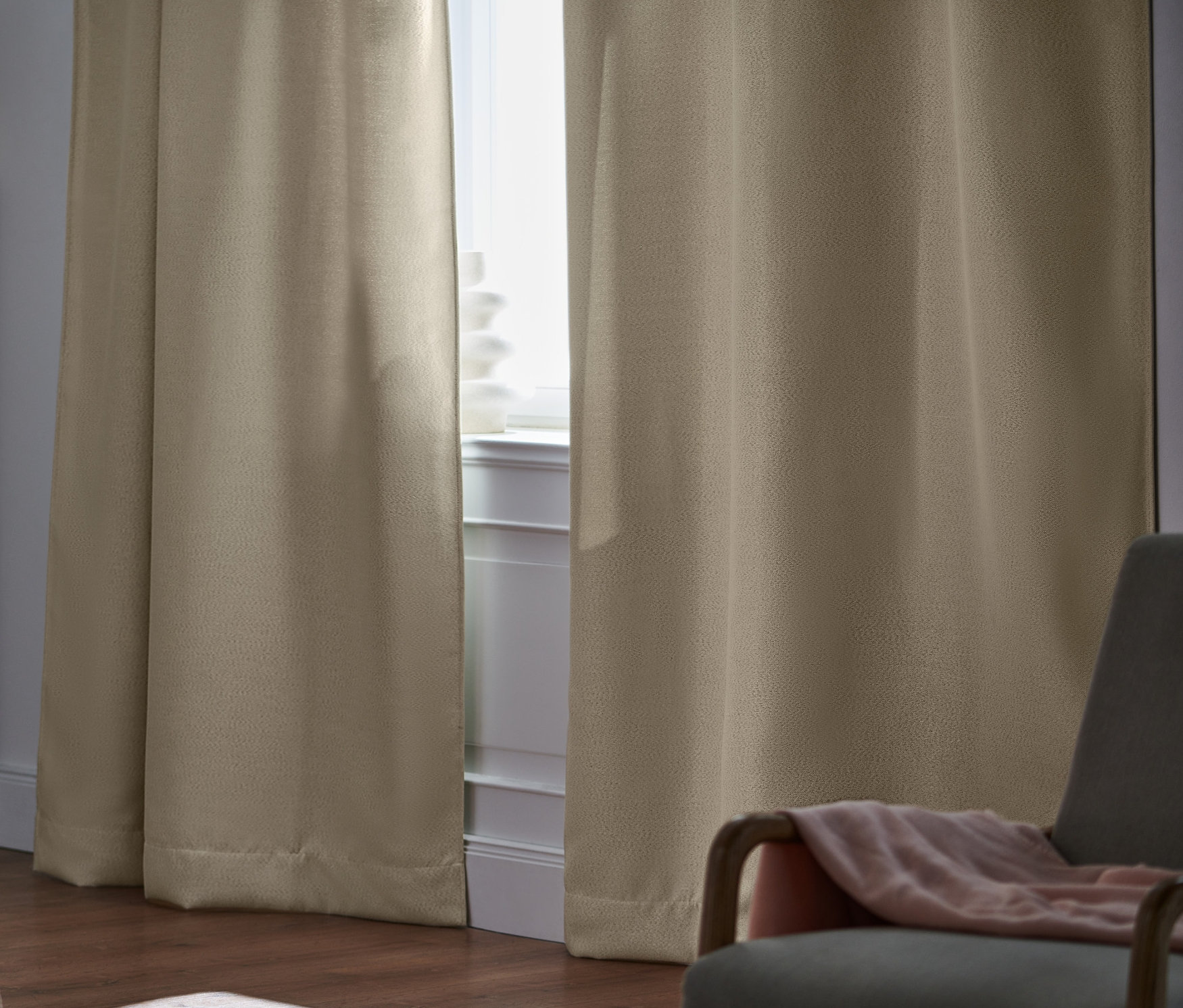 Ložnice s béžovými zatemňovacími závěsy, 2 ks u okna, postelí a šedým křeslem.