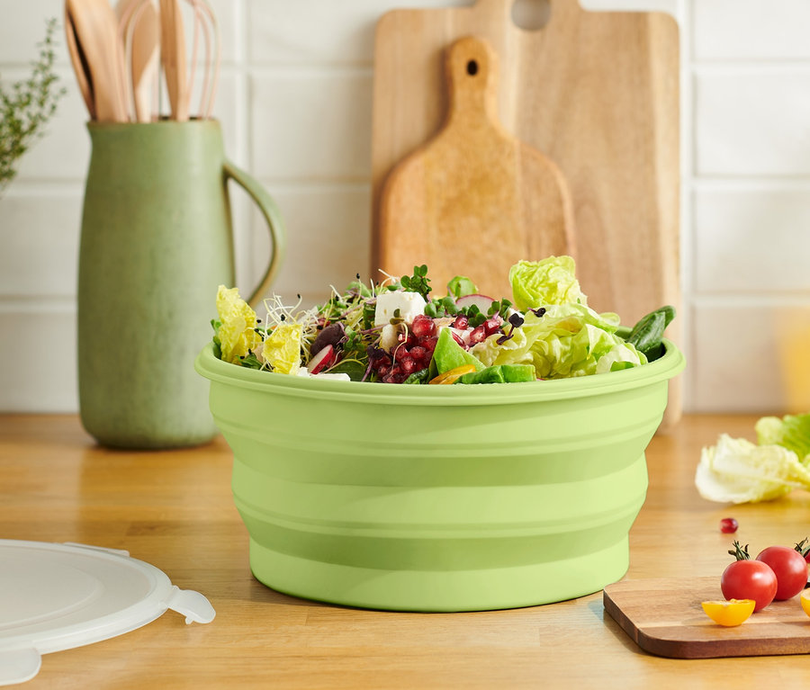 Zelená skládací salátová mísa plná salátu na dřevěné desce.