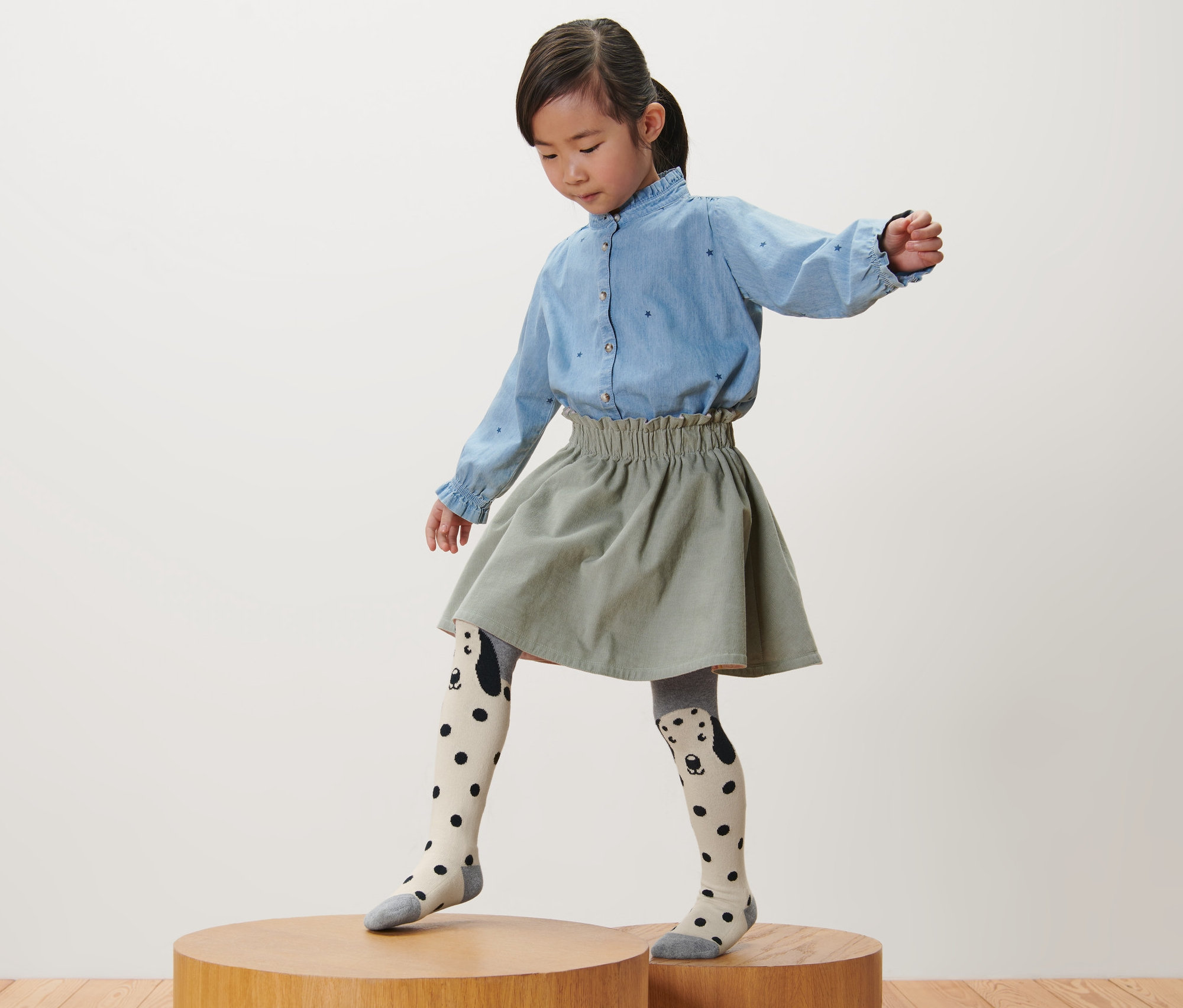 Dívka stojí na dřevěném podstavci a má na sobě růžové, šedé a bobulové dětské punčocháče, 3 ks.