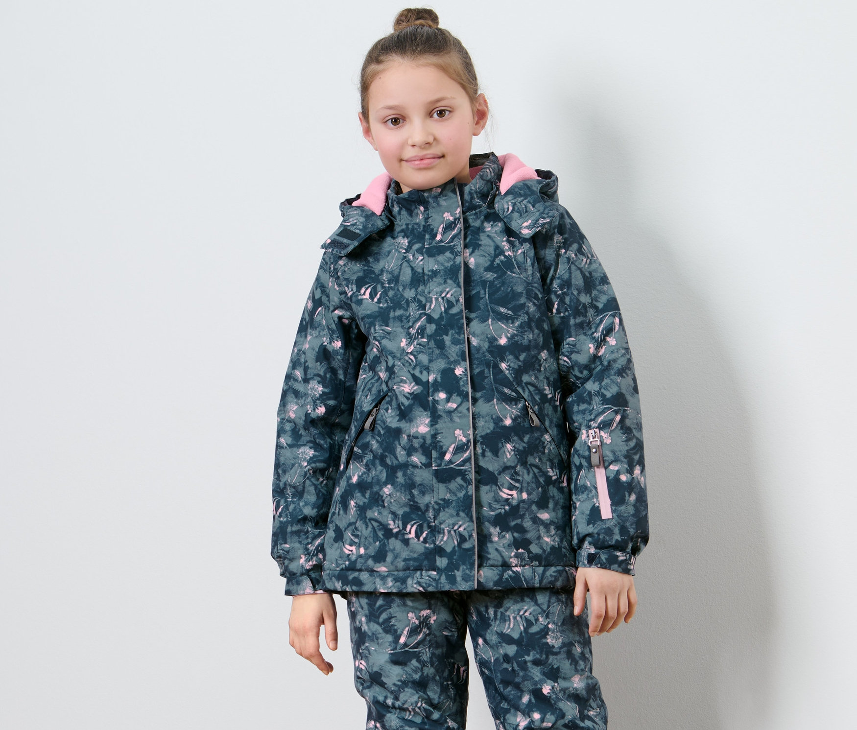 Dívka pózuje v dětské lyžařské bundě s potiskem.