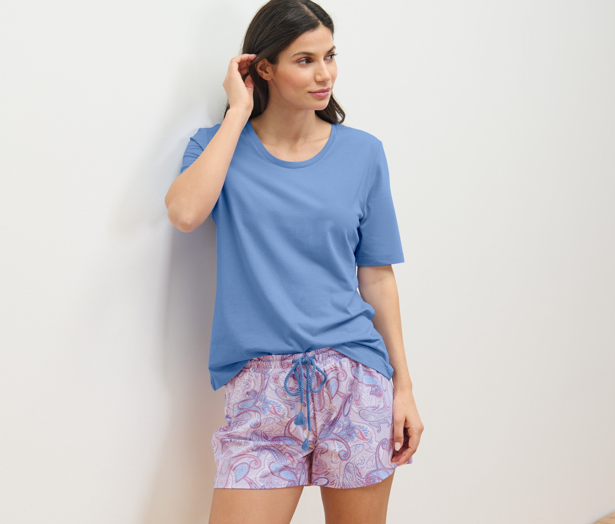 Žena v krátké pyžamové soupravě se opírá o zeď.