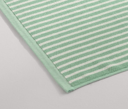 Zelená předložka do sprchy leží na podlaze vedle sprchového koutu.