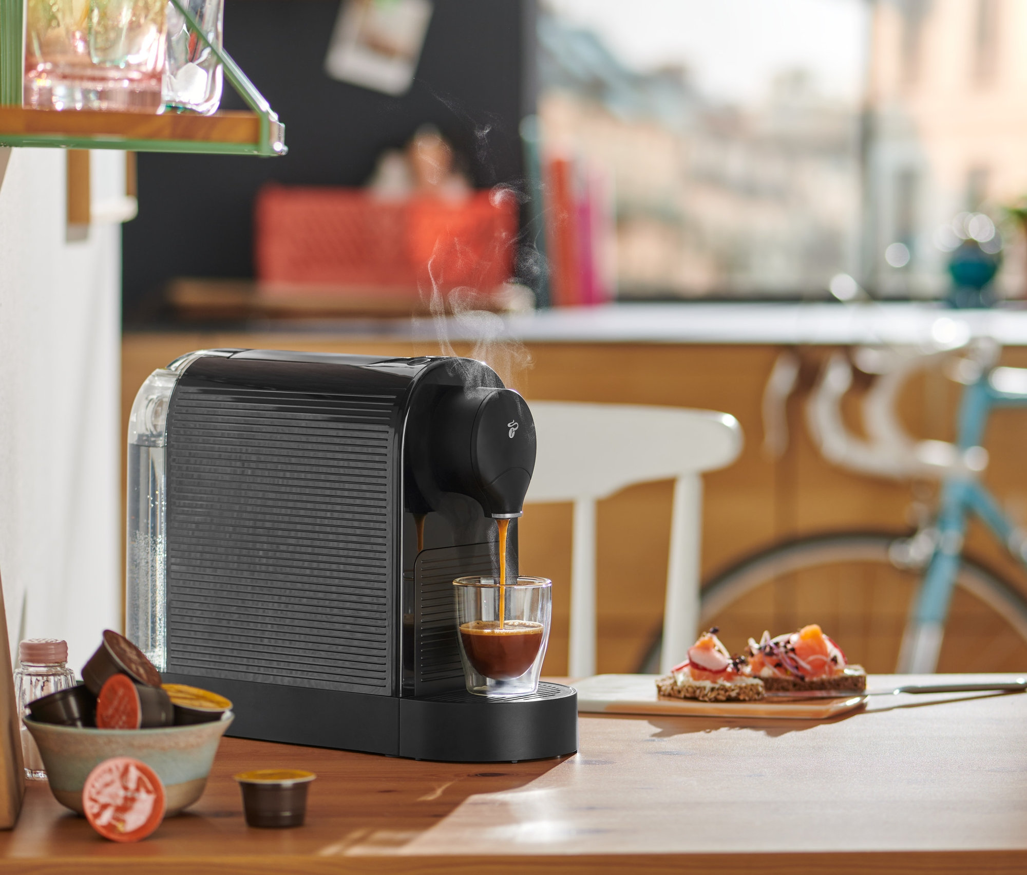 Černý kávovar Cafissimo pure+ připravuje espresso do sklenice na dřevěném stole.