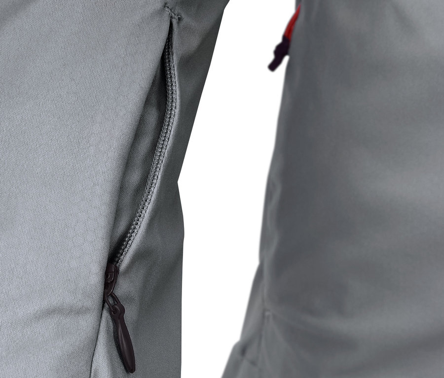 Detail světle šedé bežecké bundy se zipem na kapse.