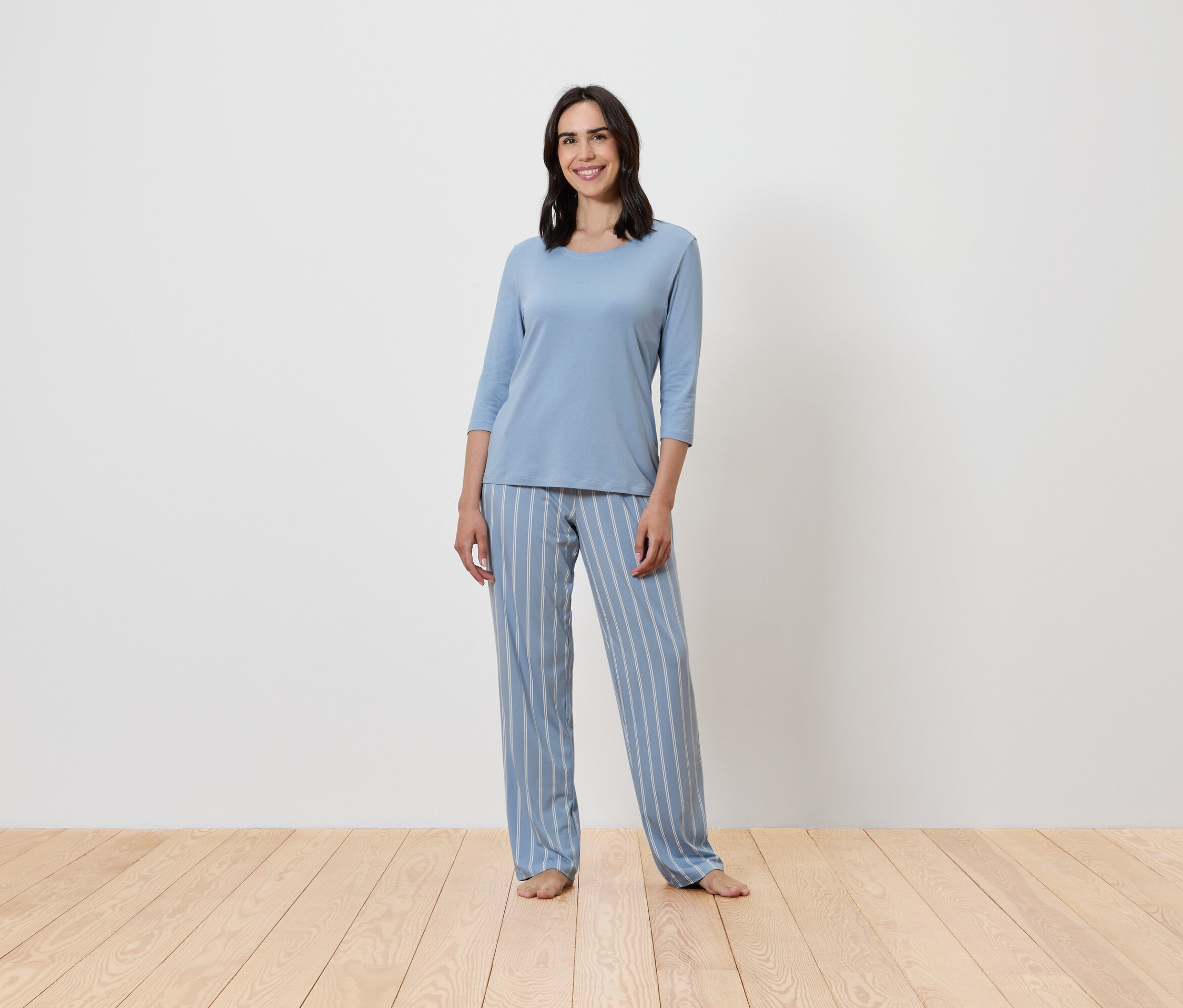 Žena stojí a má na sobě modré pyžamo s proužky.