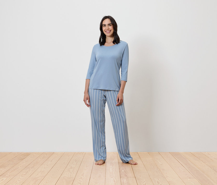 Žena stojí a má na sobě modré pyžamo s proužky.