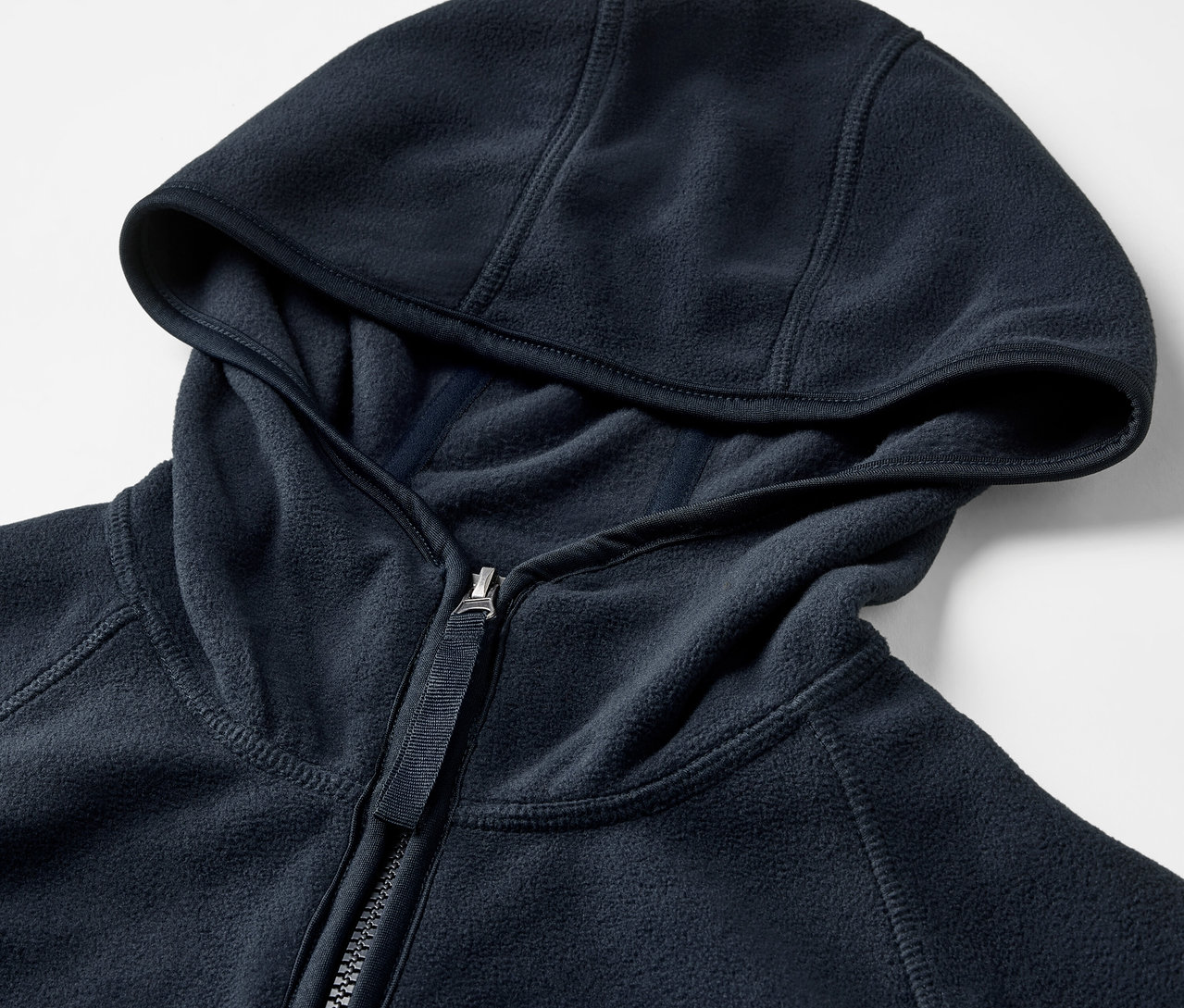 Detail modré fleecové bundy s kapucí a zipem.