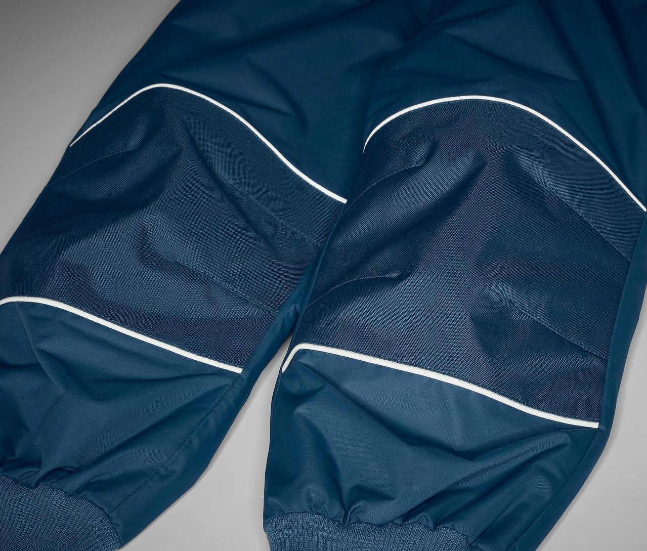 Detail dětských rostoucích kalhot do deště s reflexními prvky.