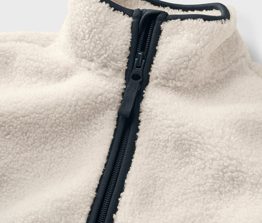 Detail dětské bundy z hebkého plyše s tmavě modrým zipem a lemováním.