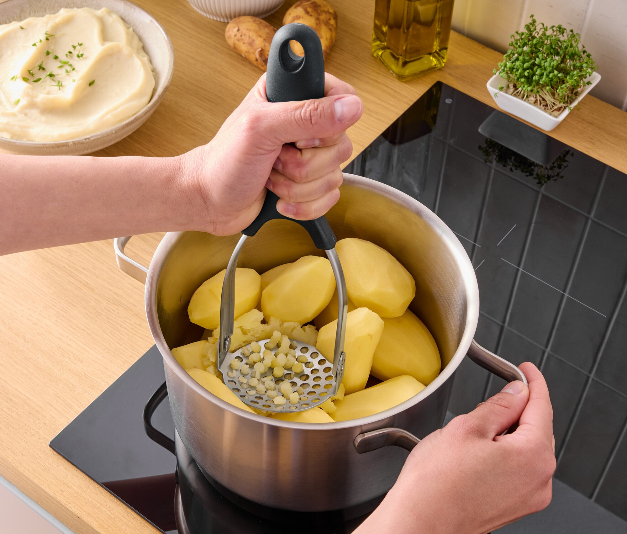 Osoba mačká vařené brambory v hrnci na sporáku s použitím mačkadla na brambory.
