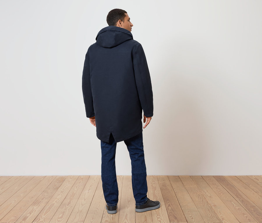 Muž zády, má na sobě tmavě modrý kabát s kapucí, džíny a boty.