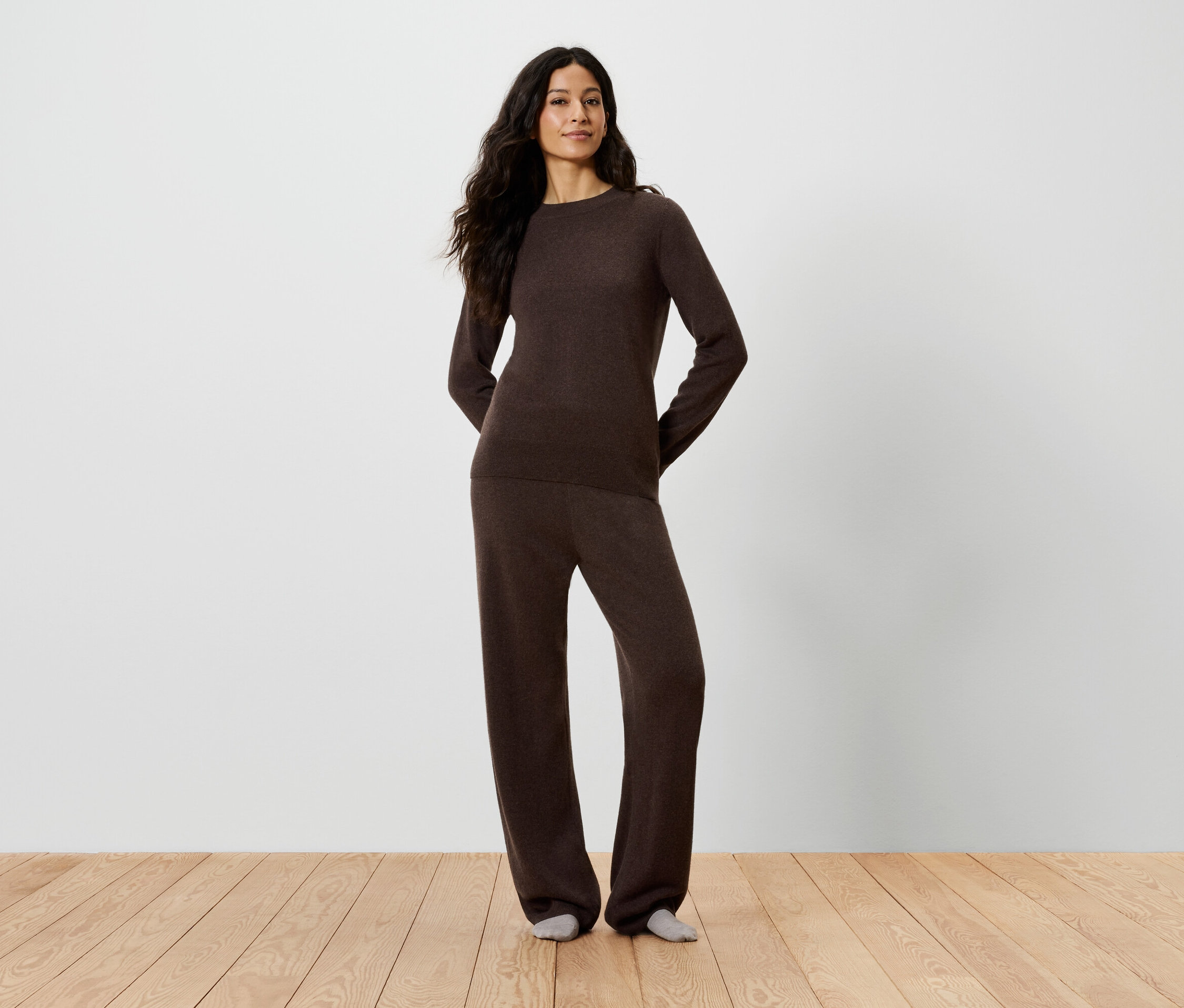 Žena pózuje v hnědém svetru a kalhotách.