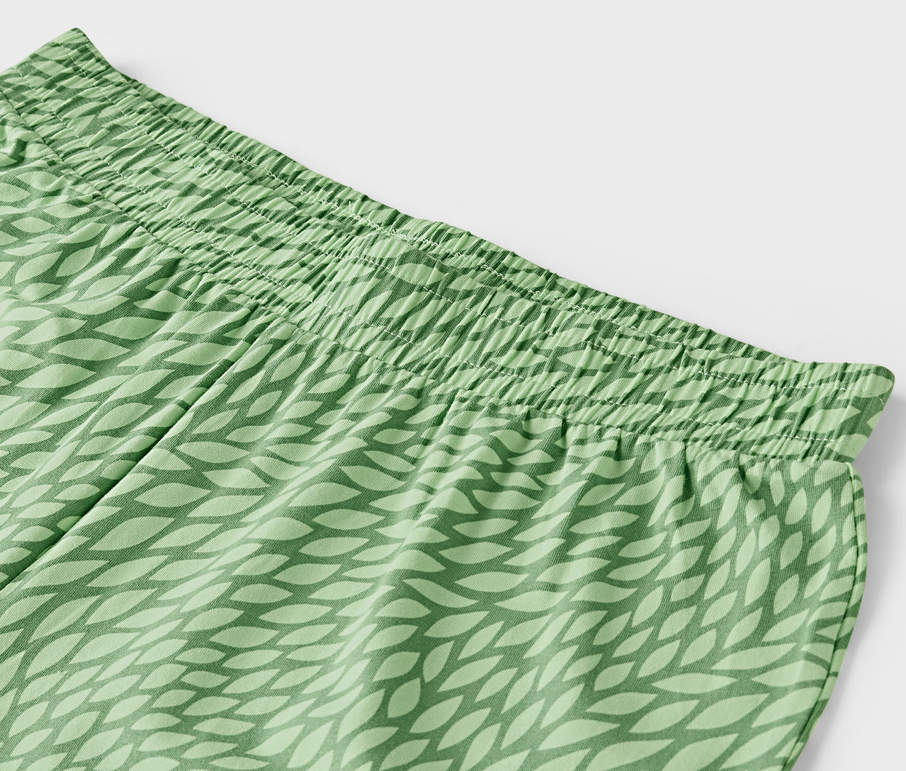 Detail zelených kalhot s elastickým pasem a vzorem lístků.