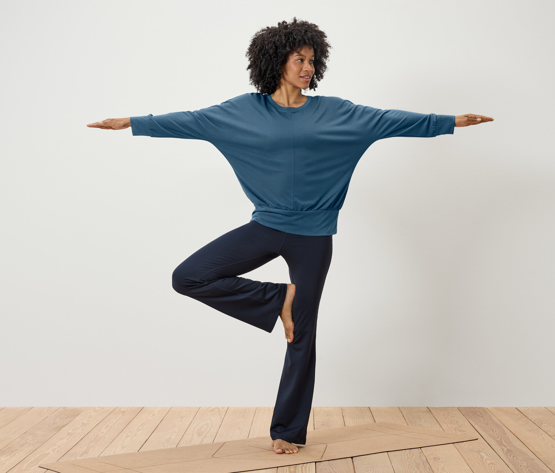 Žena cvičí jógu v modrém topu a tmavě modrých kalhotách na podložce.