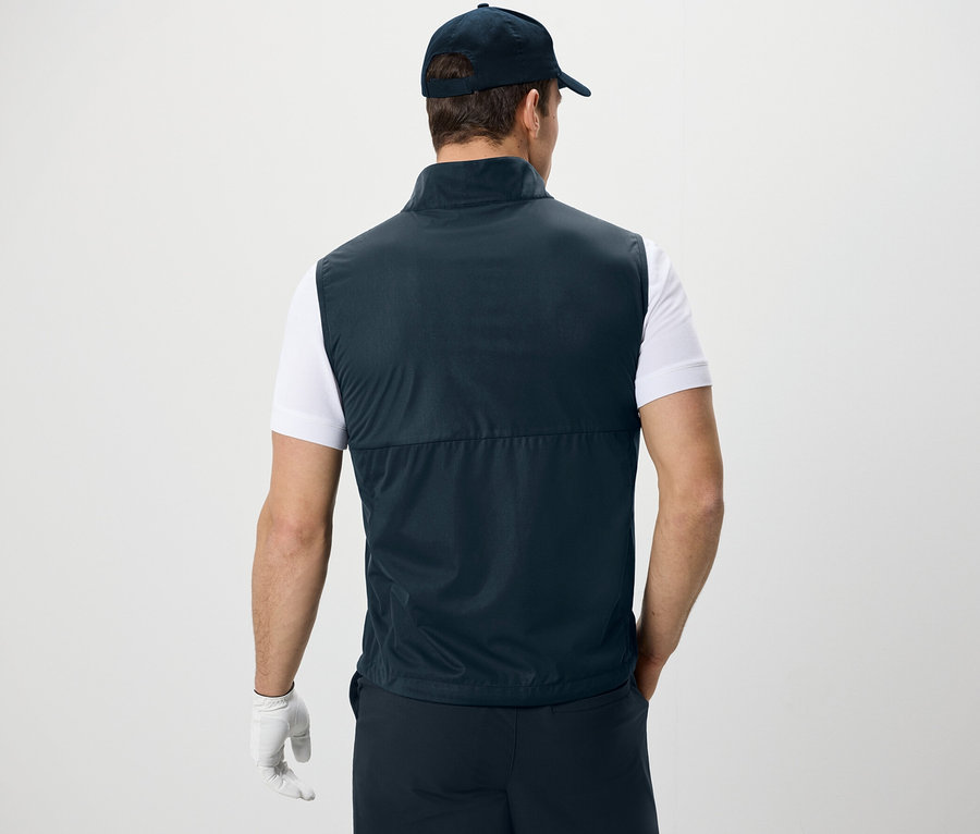 Muž zády ke kameře má na sobě softshellovou vestu, tričko a kšiltovku.