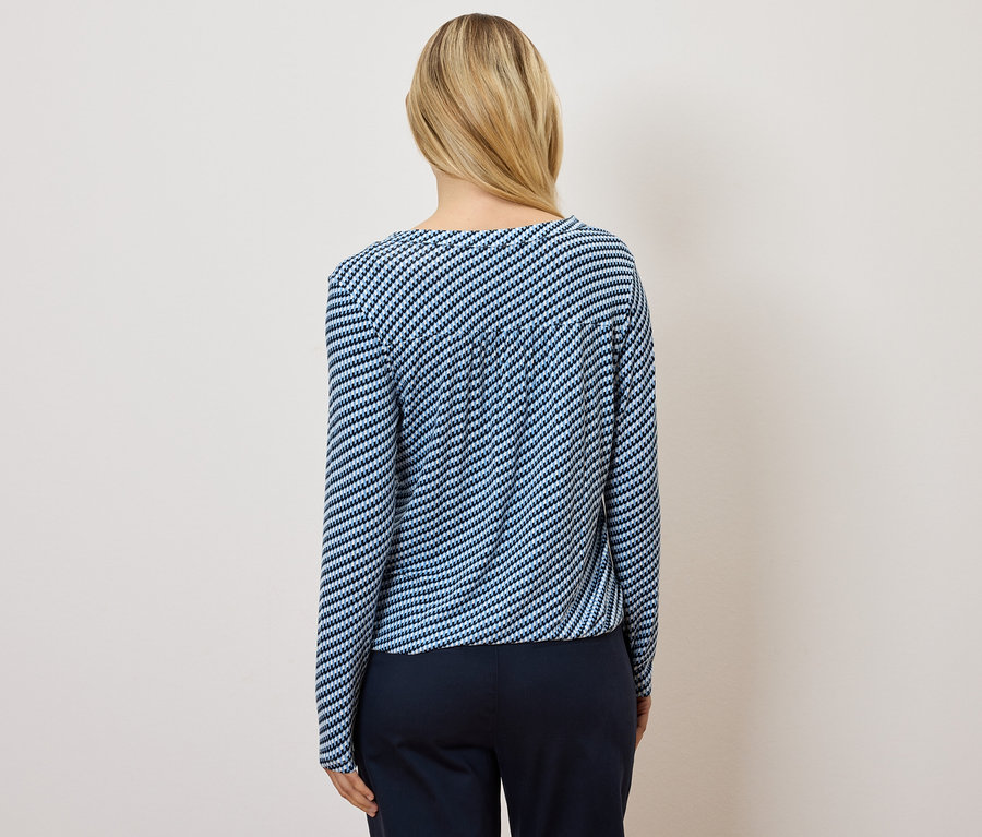 Zezadu je vidět žena s blond vlasy, má na sobě modrobílé pruhované tričko a tmavě modré kalhoty.