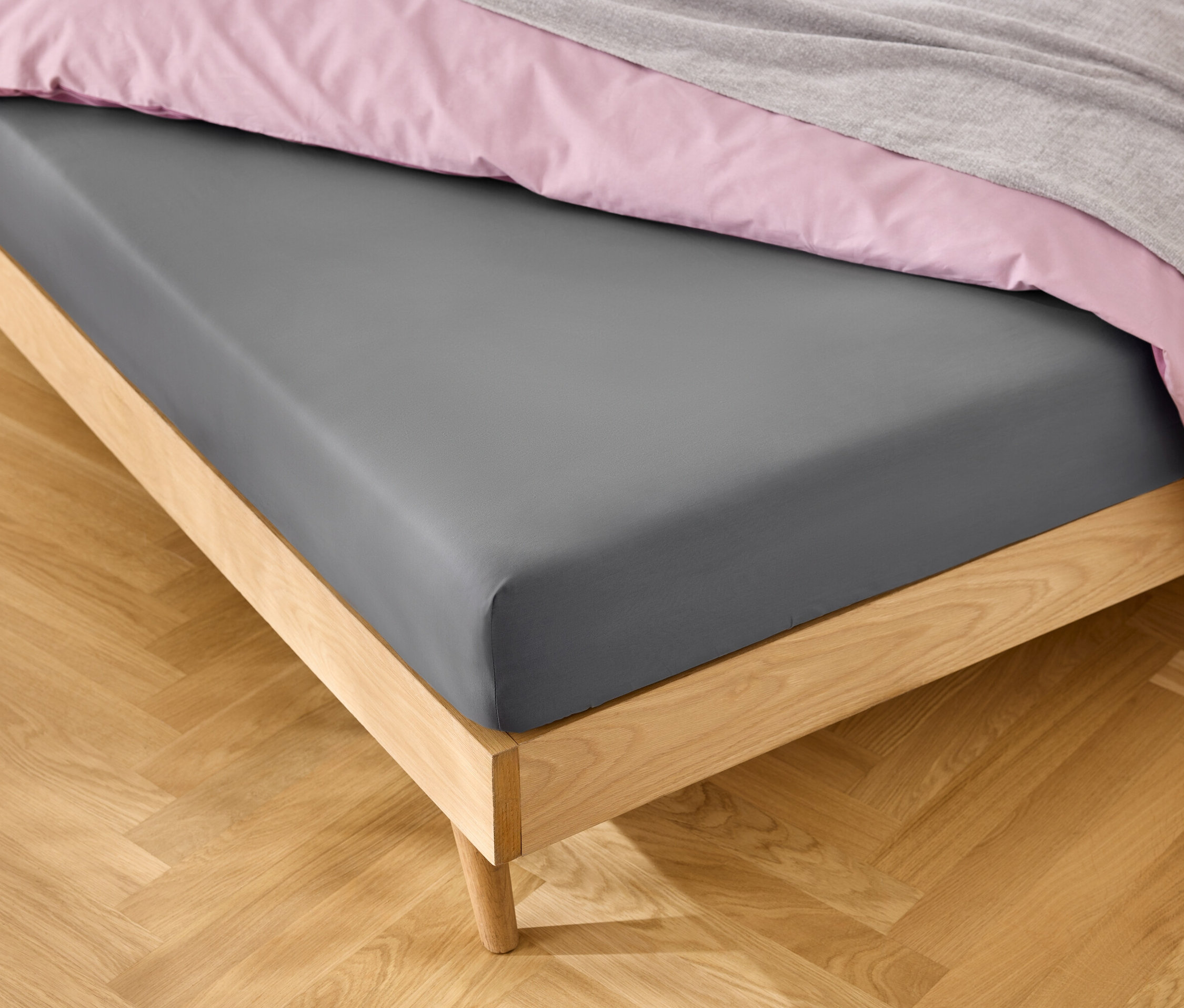 Postel s šedým prostěradlem, růžovým povlečením a šedou dekou.
