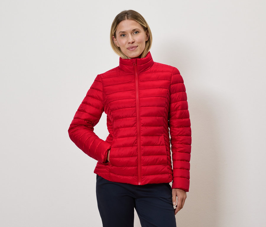 Žena pózuje v červené prošívané bundě.