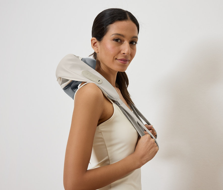 Žena se šedým a béžovým masážním přístrojem na krk přes ramena, zařízení drží v rukou.
