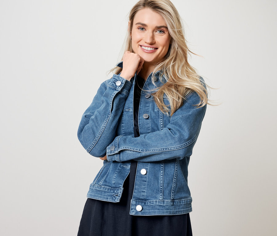 Žena pózuje v džínsové bundě a lněných šatech.