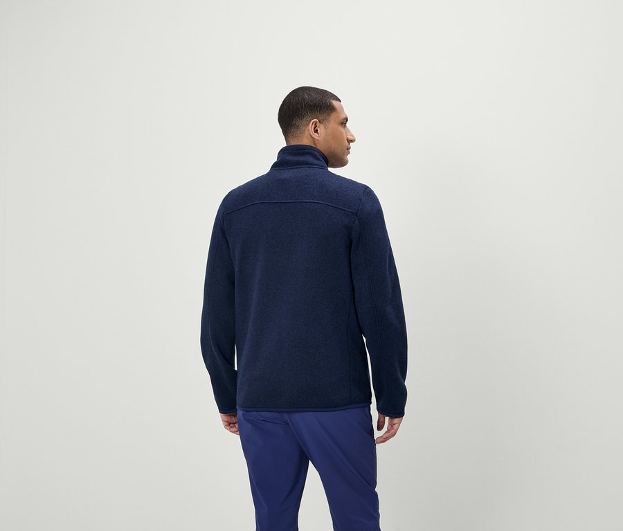 Muž má na sobě modrý svetr na zip a modré kalhoty.