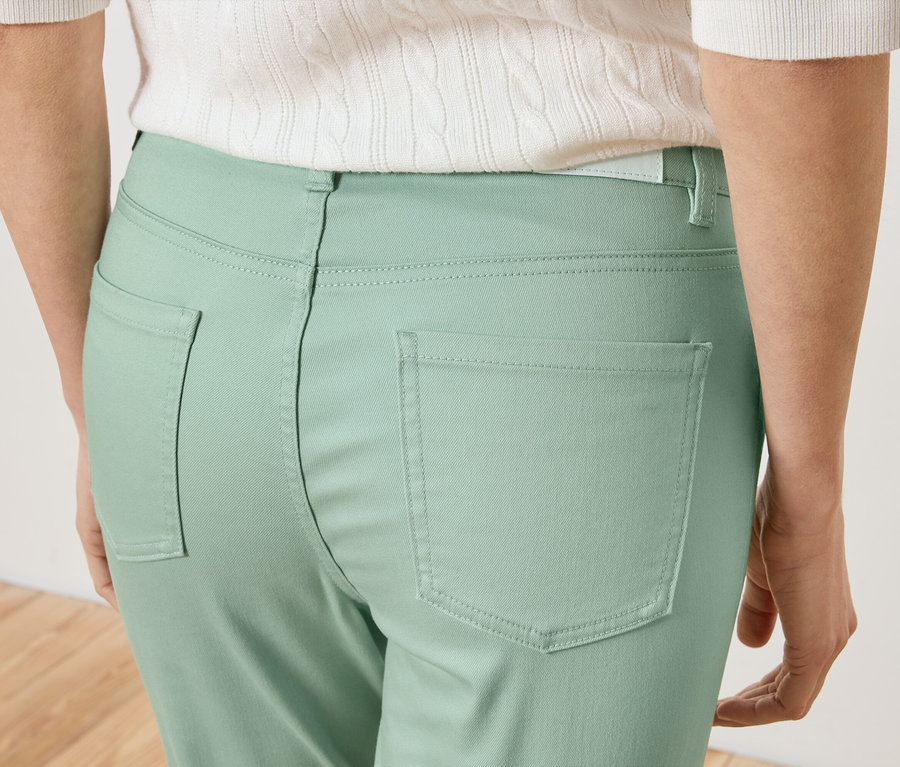 Detailní záběr na záda ženy ve světle zelených kalhotách a bílém topu.