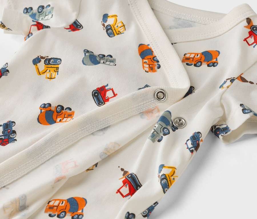 Detailní záběr na bílé dětské body s potiskem stavebních aut.