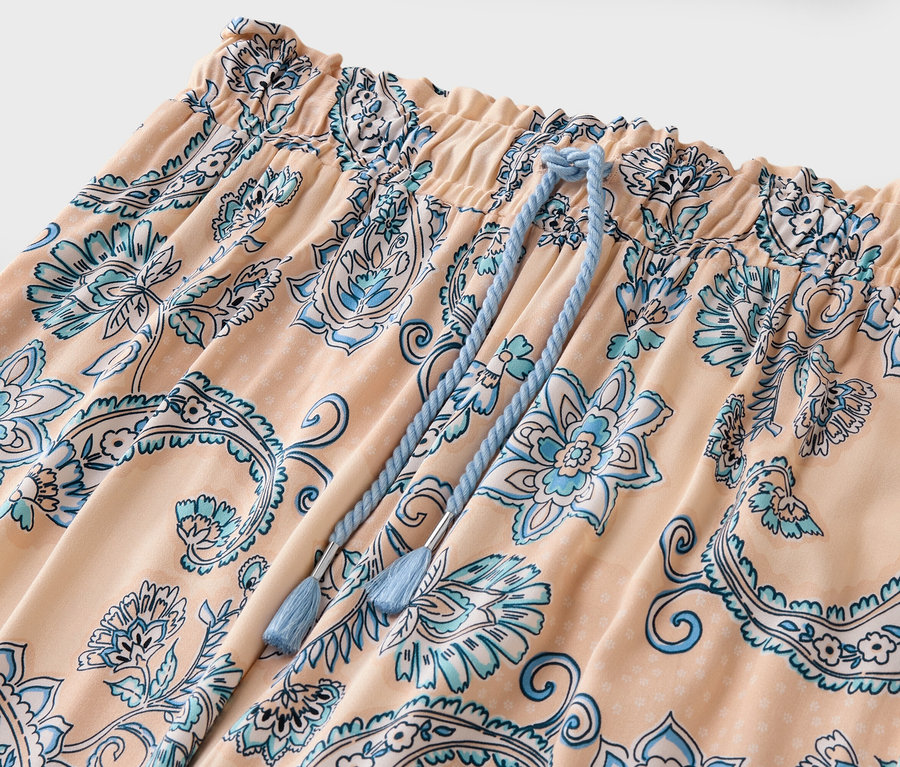 Detailní záběr broskvových kalhot s modrým květinovým vzorem a stahovací šňůrkou.