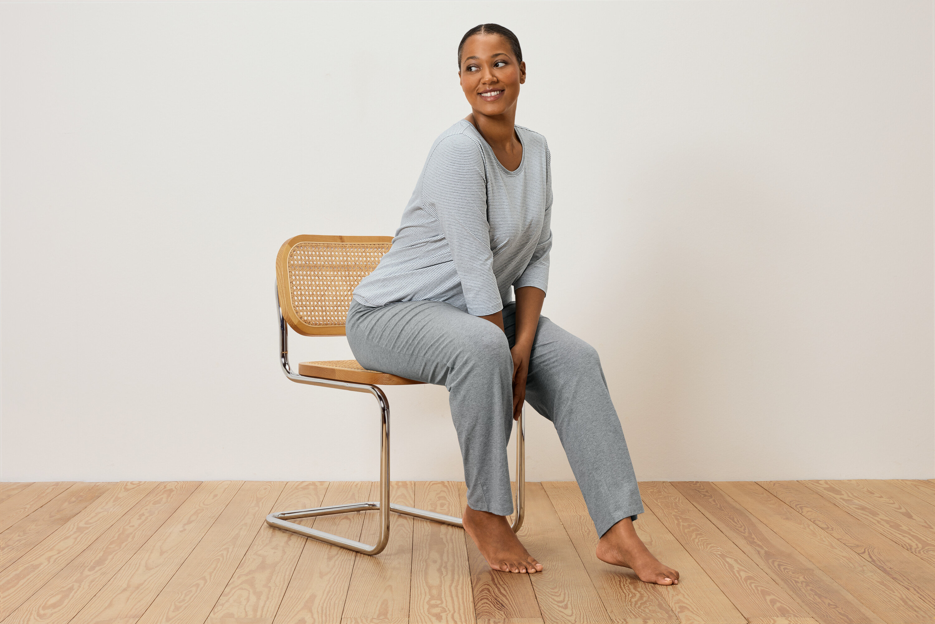 Žena sedí na židli v šedém pruhovaném pyžamu.