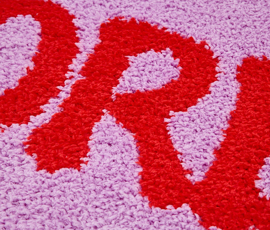 Detail fialového koberce s červeným písmenem.