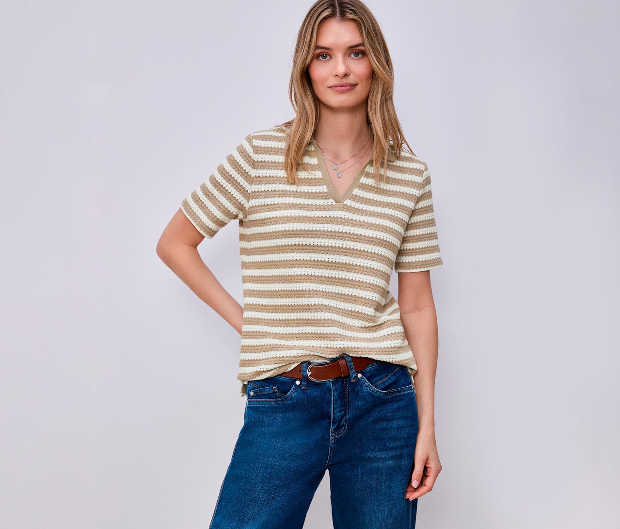 Žena s hnědým páskem a v džínách má na sobě proužkované úpletové tričko Street One. Pózuje na světlém pozadí.