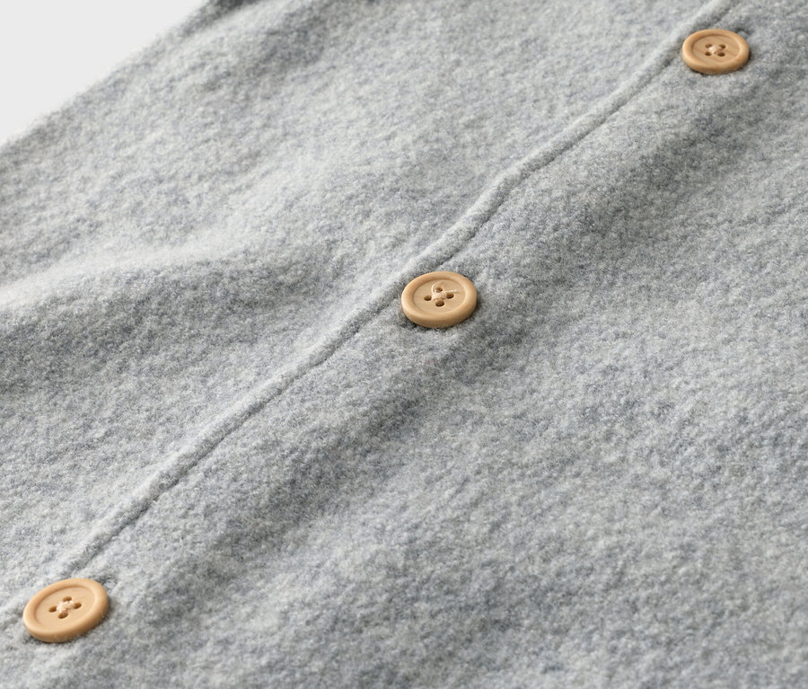 Detailní záběr na světle šedý pletený kardigan se třemi světle hnědými knoflíky.