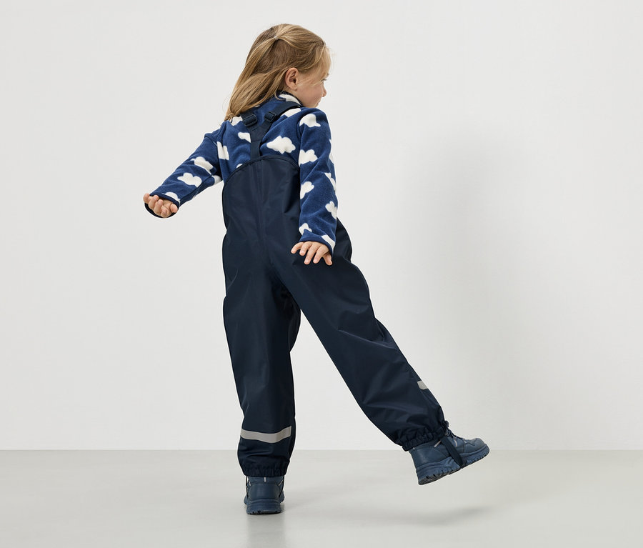 Dívka v tmavě modrých nepromokavých kalhotách a modrém svetru s oblačným vzorem, pohled zezadu.