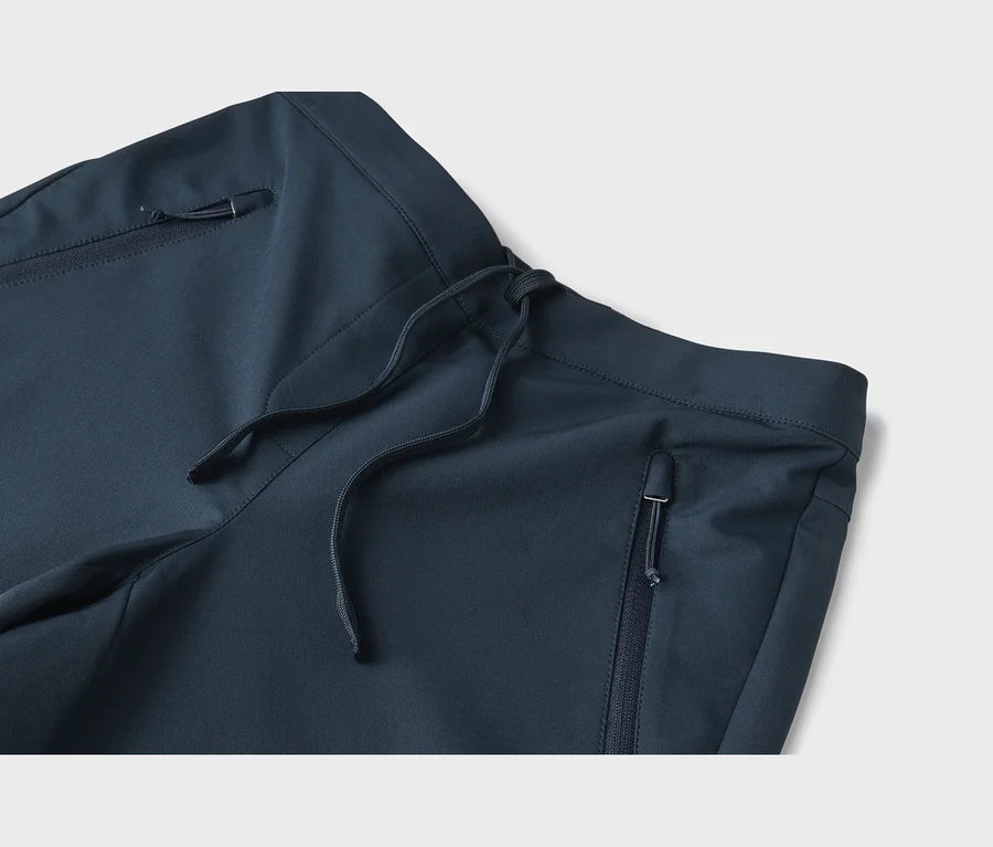 Detail tmavě modrých kalhot se stahovací šňůrkou v pase a kapsami na zip.