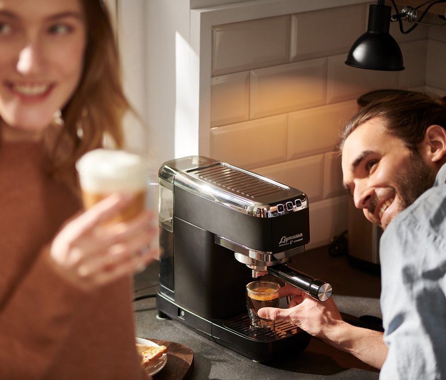 Muž připravuje espresso na pákovém kávovaru Lapressa černý, žena drží latte.
