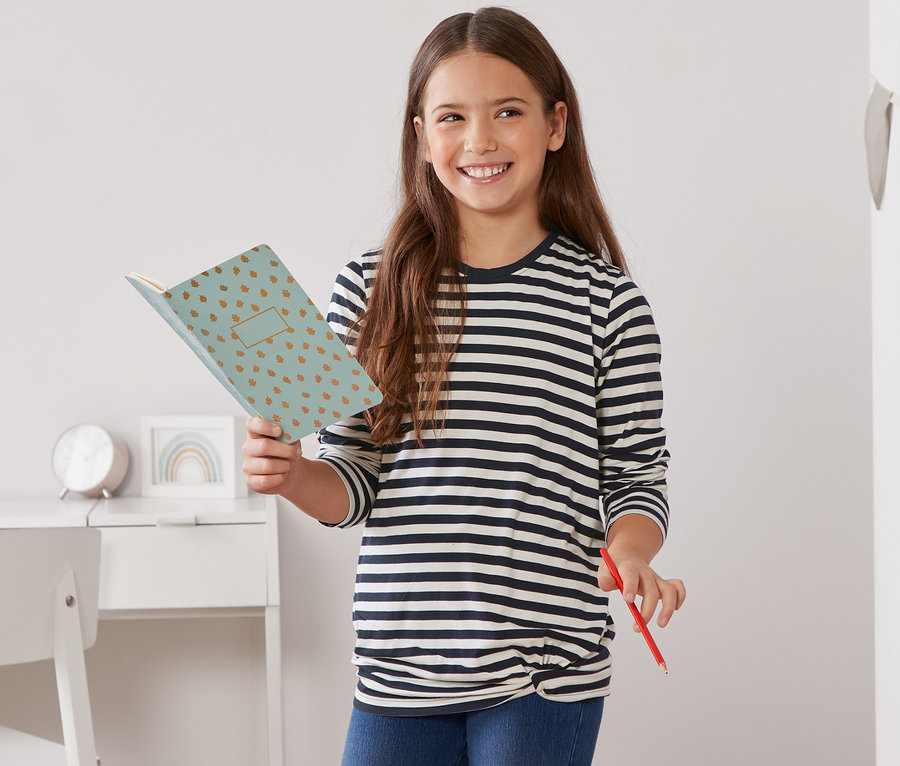 Dívka drží otevřený zápisník a červenou tužku. Má na sobě modro-bílé proužkované triko s dlouhým rukávem a ozdobným uzlem.