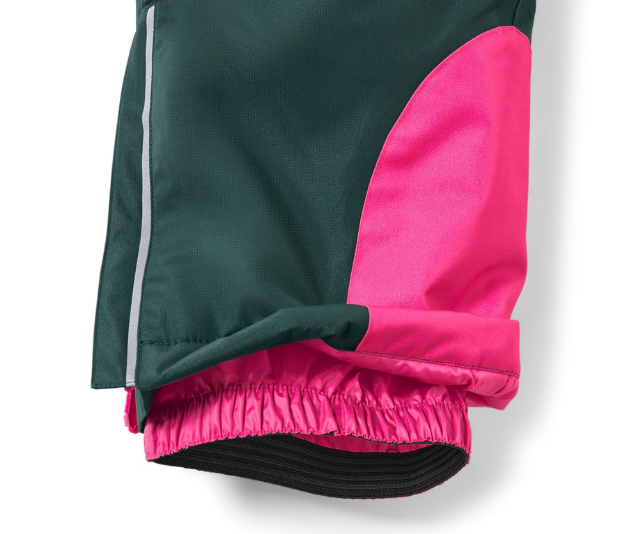 Detail dětských lyžařských kalhot tmavě zelené barvy s růžovým panelem na nohavici a elastickým lemem.