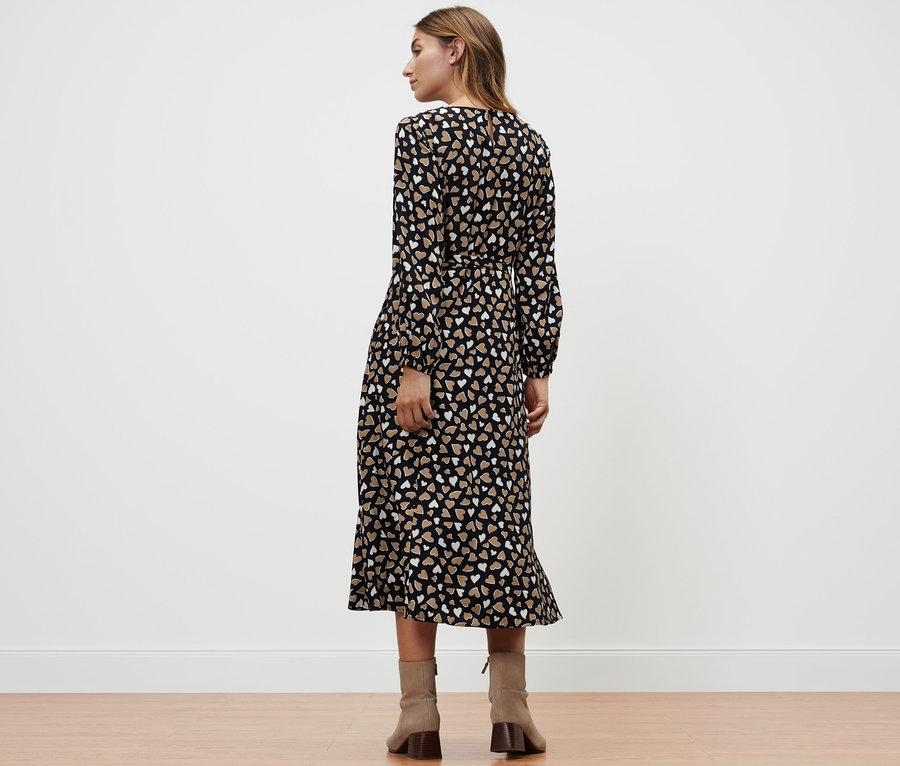 Žena stojí zády a má na sobě tkané šaty s celopotiskem.