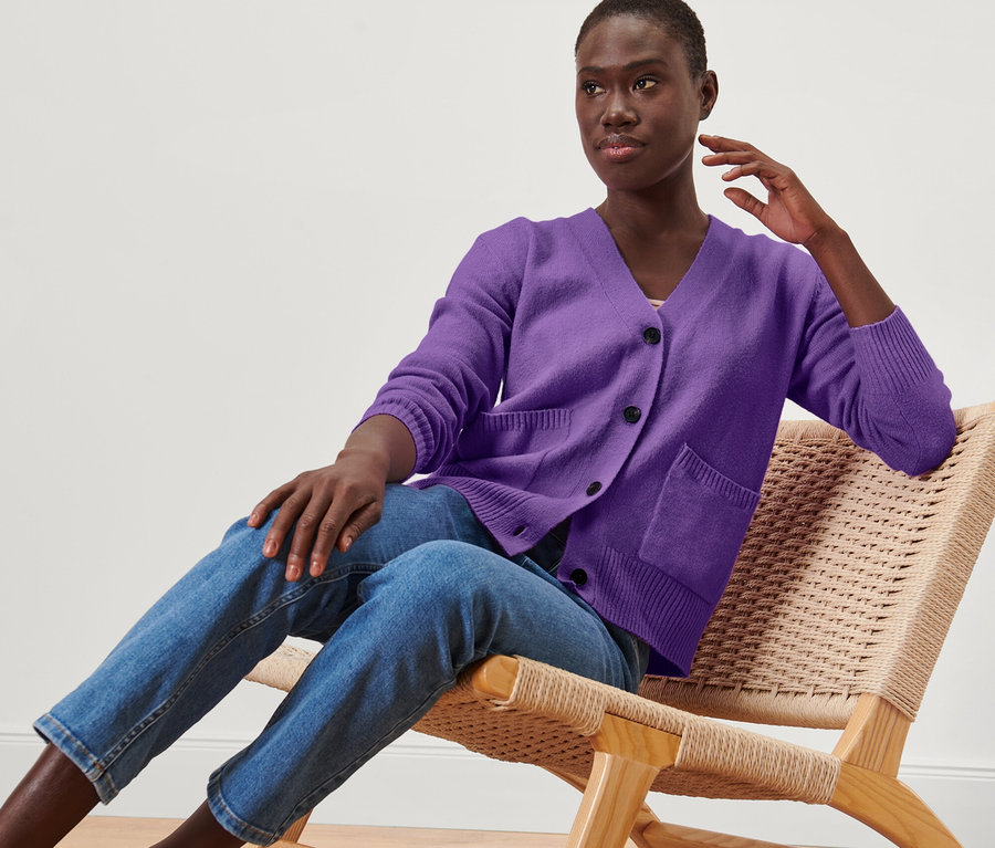 Žena sedí na židli a má na sobě fialový pletený svetr s vlnou.