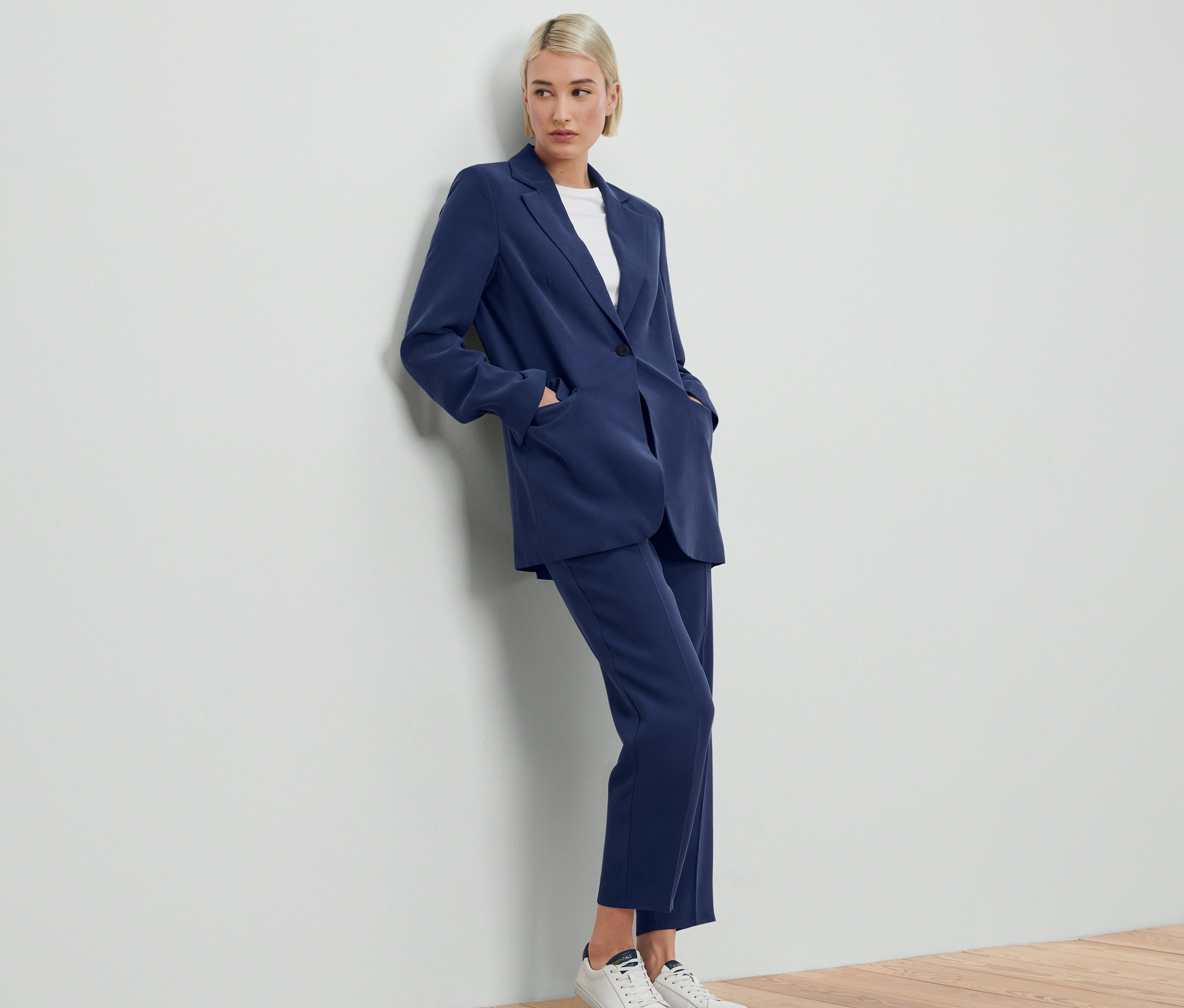 Žena opřená o zeď má na sobě modré sako a kalhoty Tkaný blejzr.