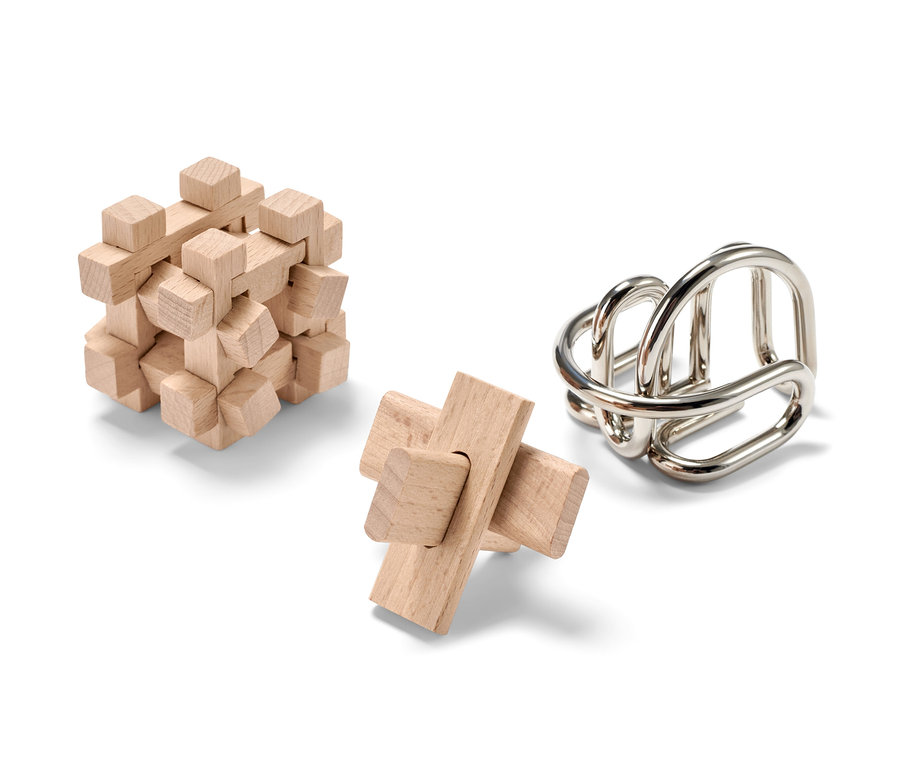 Tři hlavolamy na bílém pozadí. Dva dřevěné a jeden kovový.