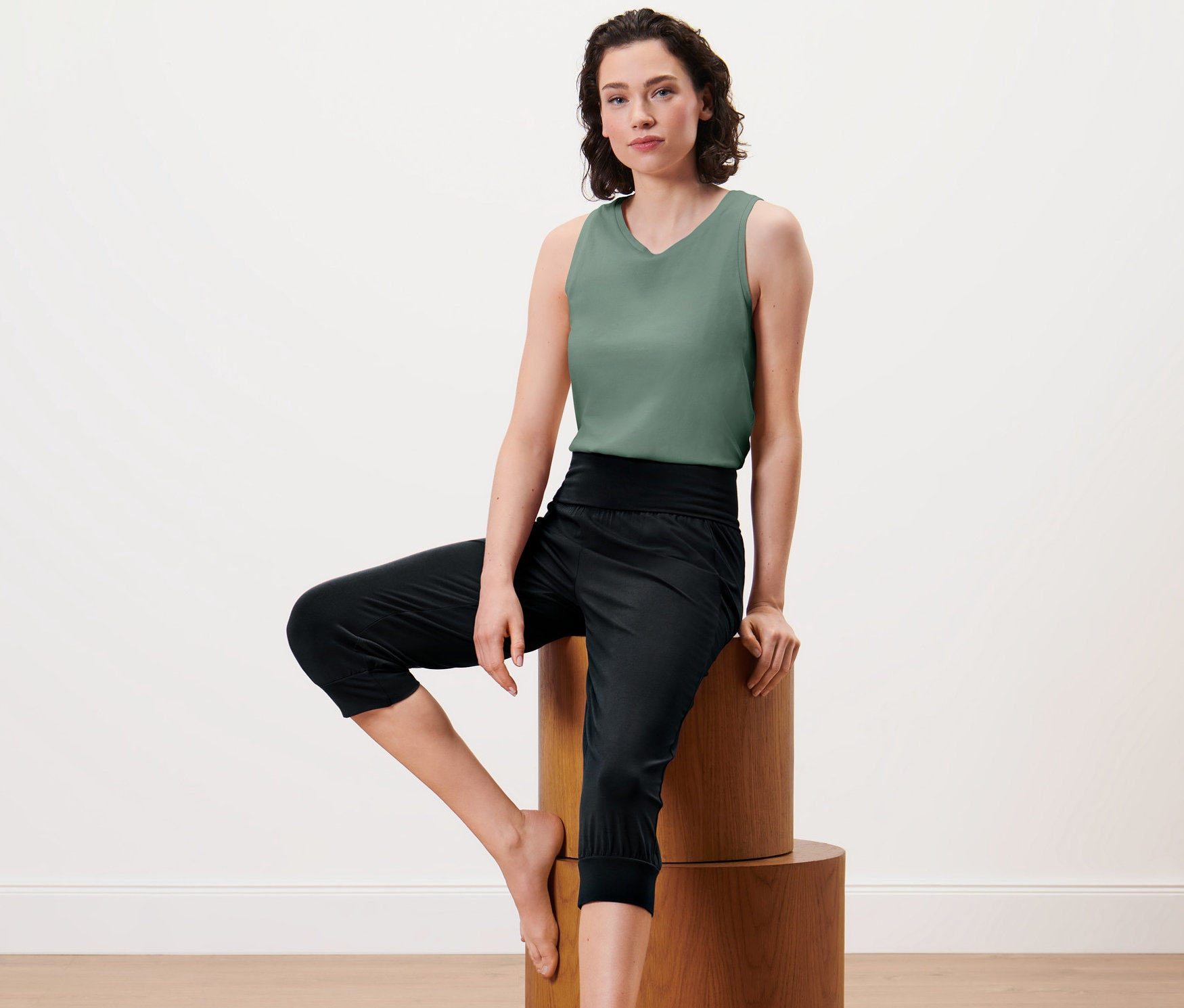 Žena sedí na dřevěném podstavci a má na sobě 3/4 kalhoty na jógu.