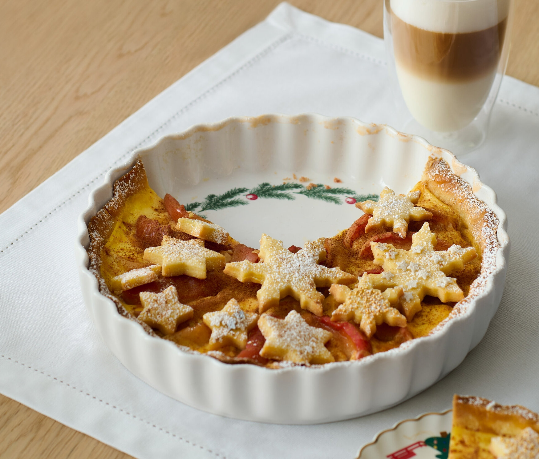 Koláč ve formě na koláč s hvězdami z těsta a sklenice latté.