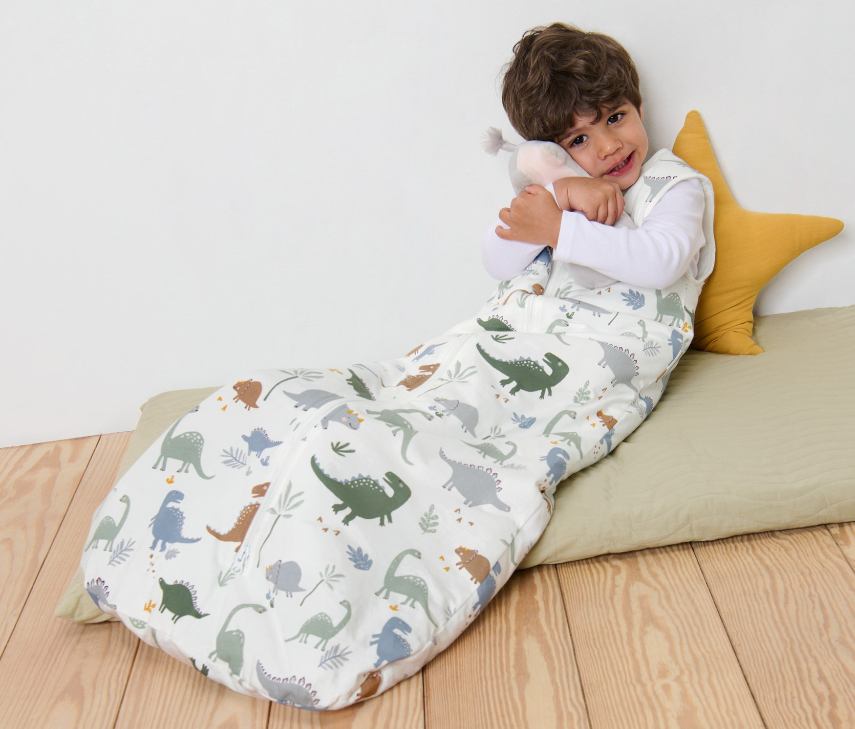 Chlapec leží v spacím pytli 3 TOG, 110 cm s dinosauřím vzorem a objímá plyšovou hračku.