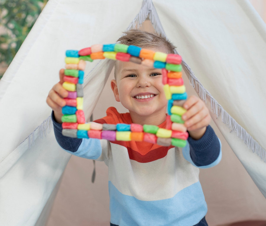 Chlapec sedí v teepee a drží v rukou barevný čtverec ze sady PlayMais®.