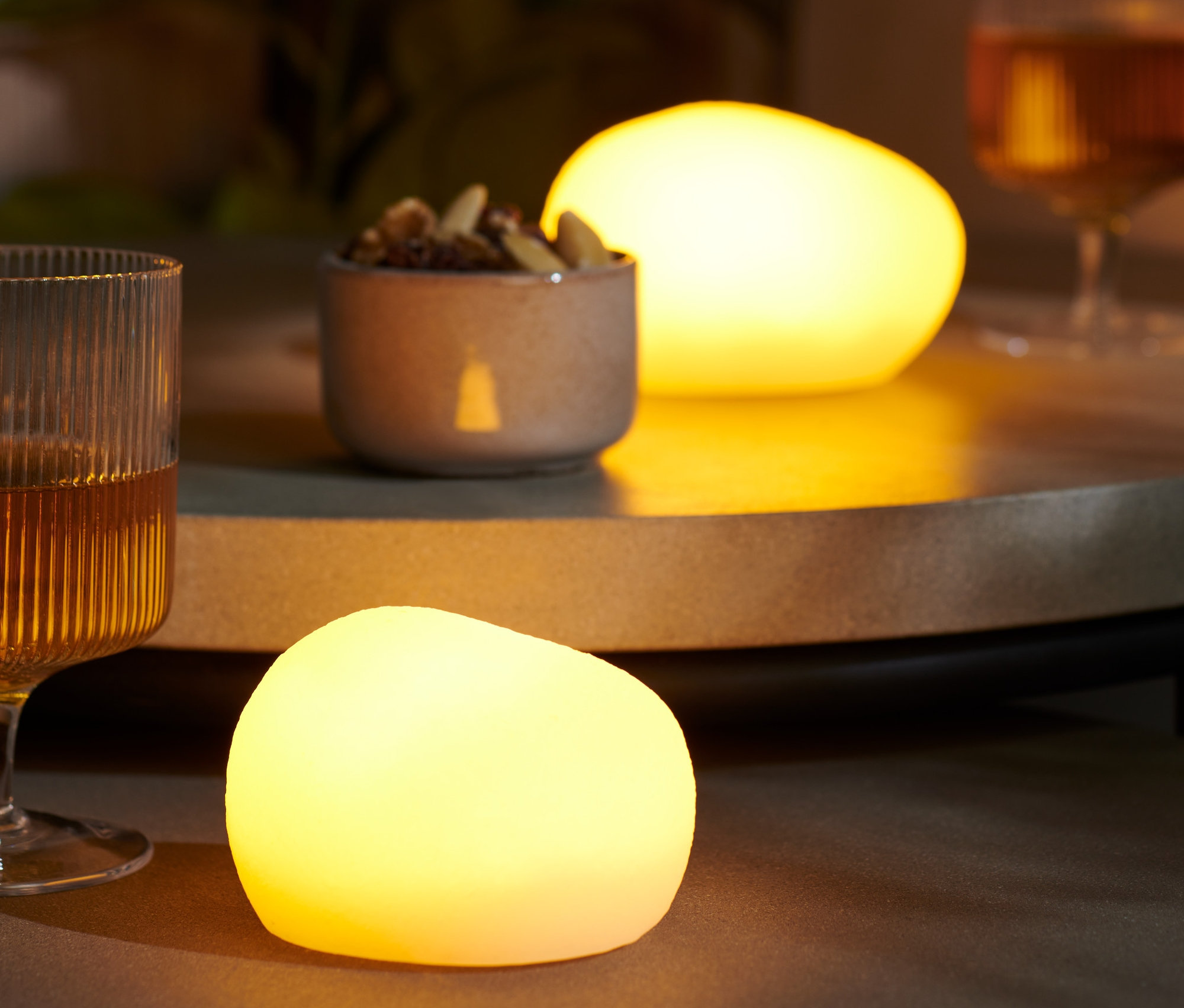 Na stole stojí dvě LED dekorační kameny, sklenice s pitím a miska oříšků.