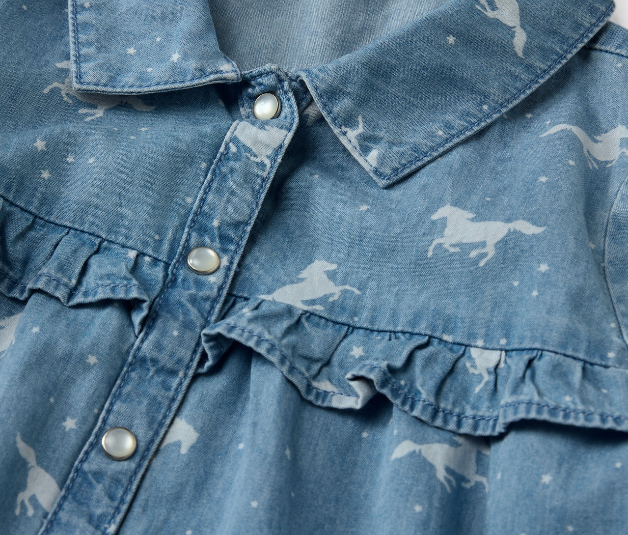 Detail dětských džínových šatů s potiskem koní a volánky.