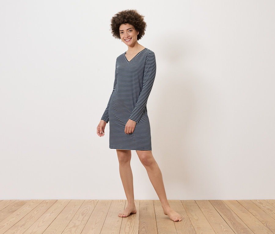 Žena stojí na dřevěné podlaze a má na sobě pruhované šaty s dlouhým rukávem.