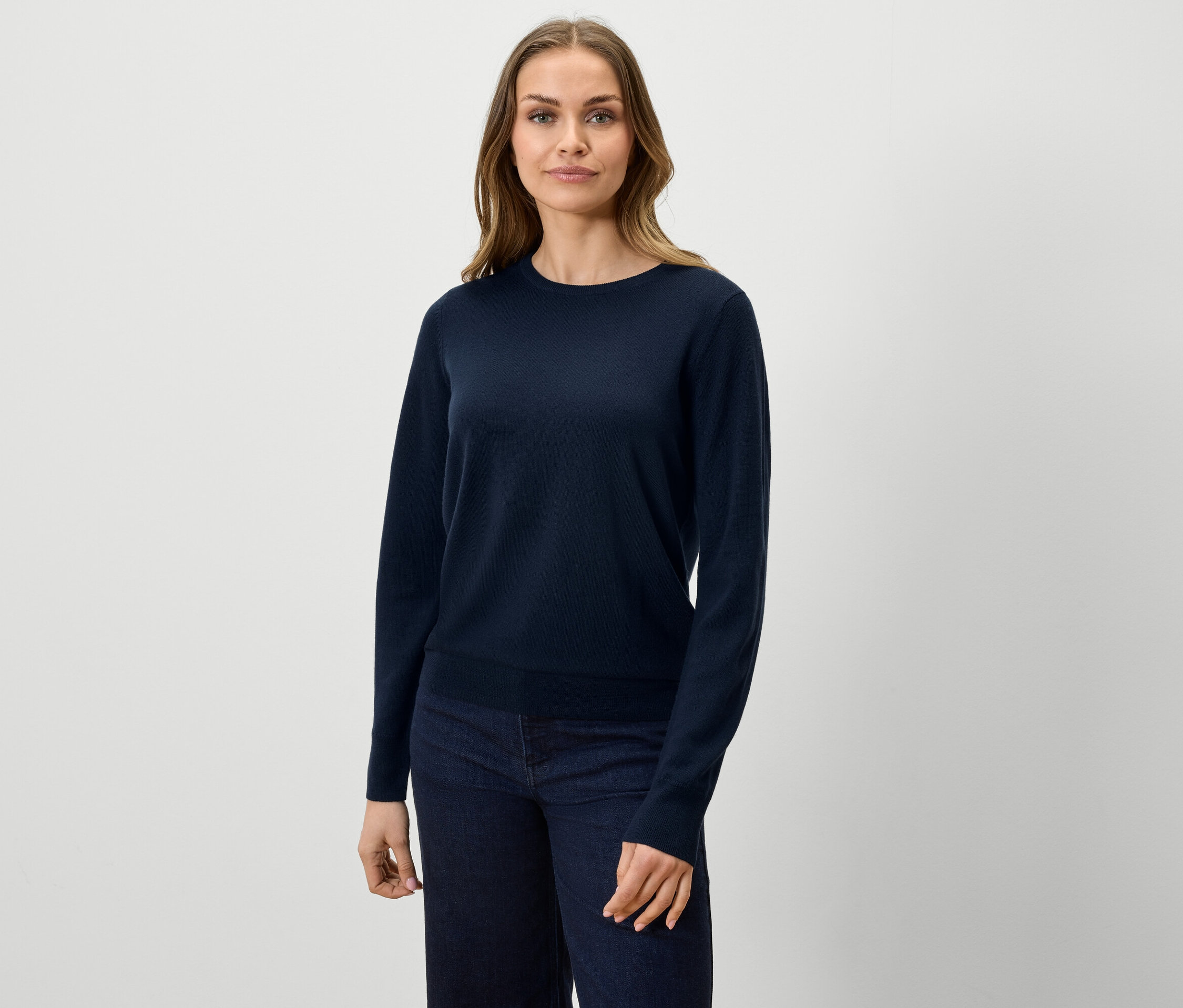 Žena má na sobě tmavě modrý svetr a džíny.