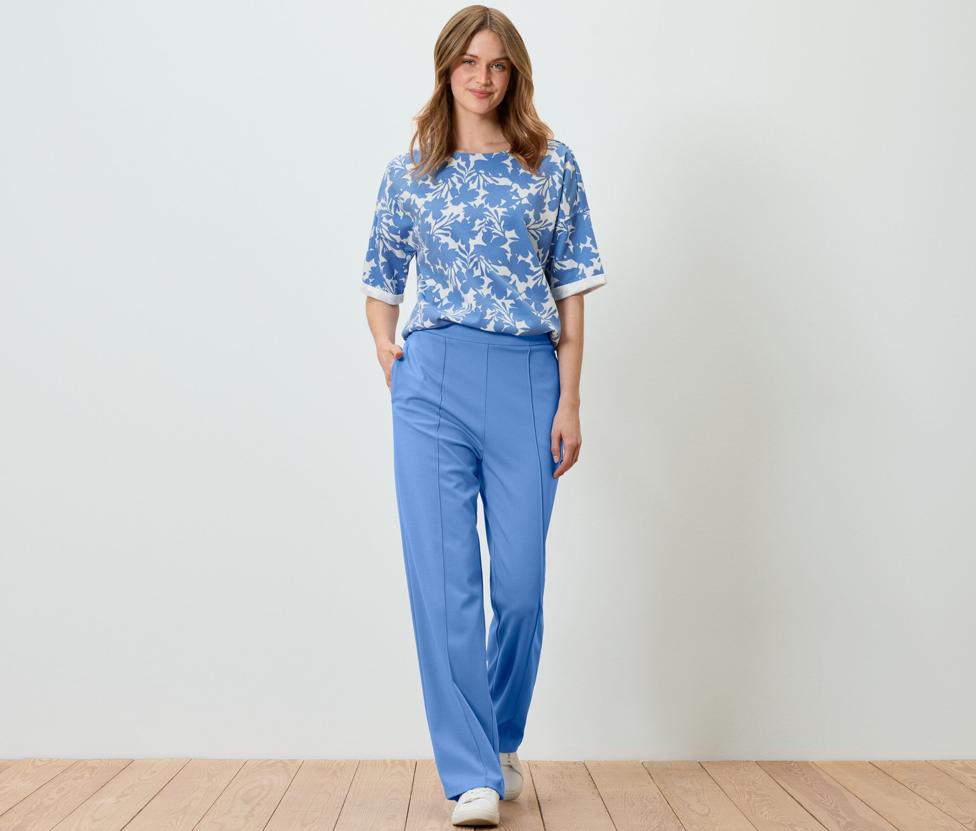 Žena pózuje v světle modré mikině s potiskem a modrých kalhotách.